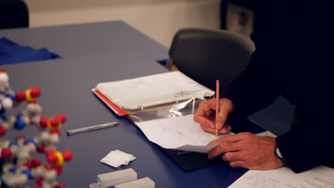 a college science professor grading homework assignments from his students and taking notes in his binder during a semester