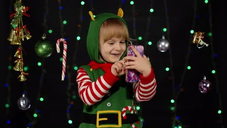 Kid-girl-Christmas-elf-Santa-helper-types-something-on-mobile-phone-enjoys-browsing-social-media