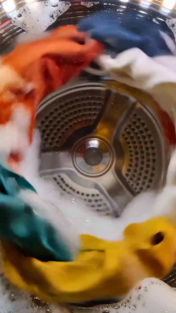 Vertical video: Wash cycle starting, rotating wet laundry ring in steel drum, cleaning with suds