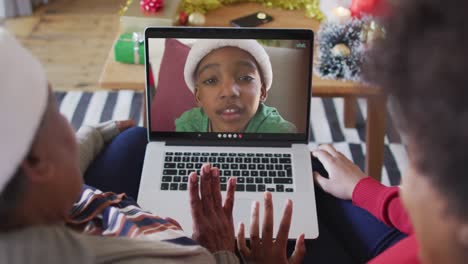 madre y hija afroamericanas usando una computadora portátil para una videollamada de navidad con un niño en la pantalla