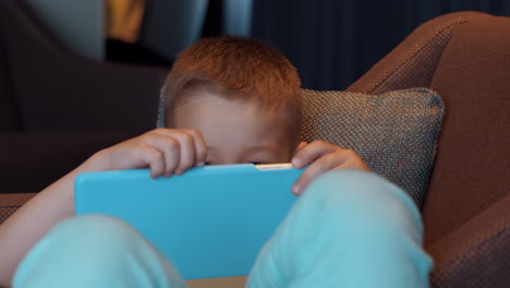 Child-lying-in-arm-chair-and-watching-cartoons-on-pad