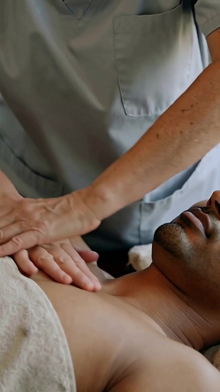 Vertical video: Contact starting therapist pressing palms to man chest on table in scrubs for care