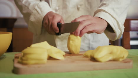 boy hands cut potatoes into logs on a wooden cutting board in private kitchen