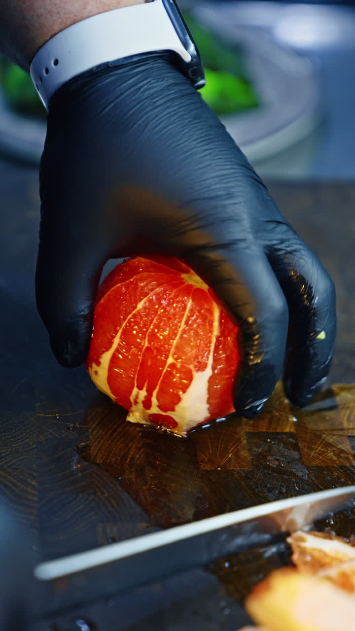 Male cook's hands in latex gloves peels the orange with a sharp knife. Cooking concept close up. Vertical video.
