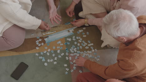 top view of group of unrecognizable people sitting on carpet on floor, doing puzzle
