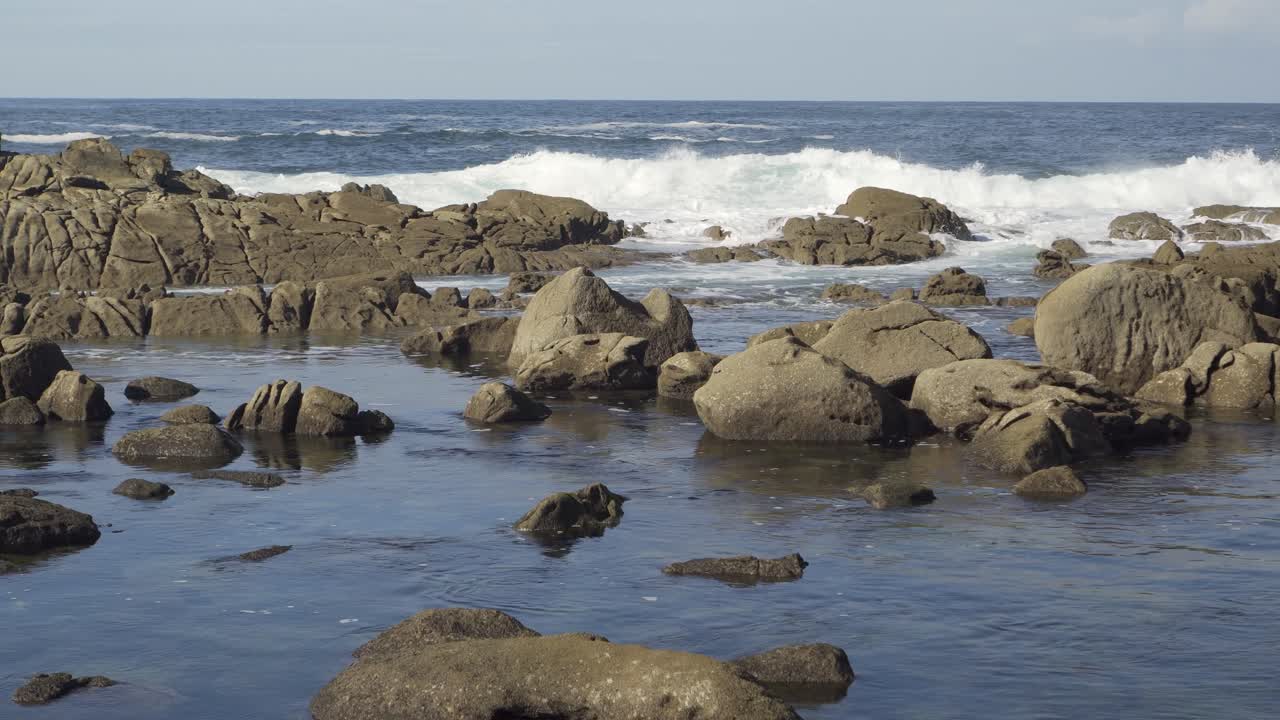 Static shot of blue waves breaking on a rocky shore with seawater around them