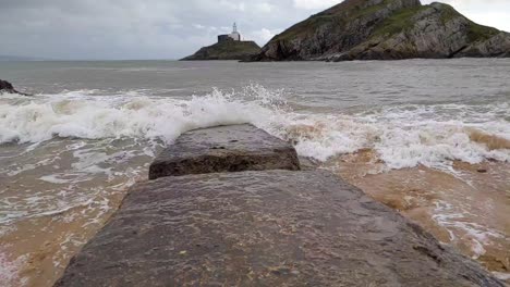 Las-Olas-Del-Mar-Agitado-En-Cámara-Lenta-Golpean-El-Embarcadero-Erosionado-Con-El-Faro-De-La-Isla-En-El-Fondo