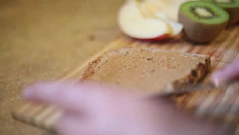 slow motion shot of someone spreading peanut butter onto a piece of whole wheat bread toast