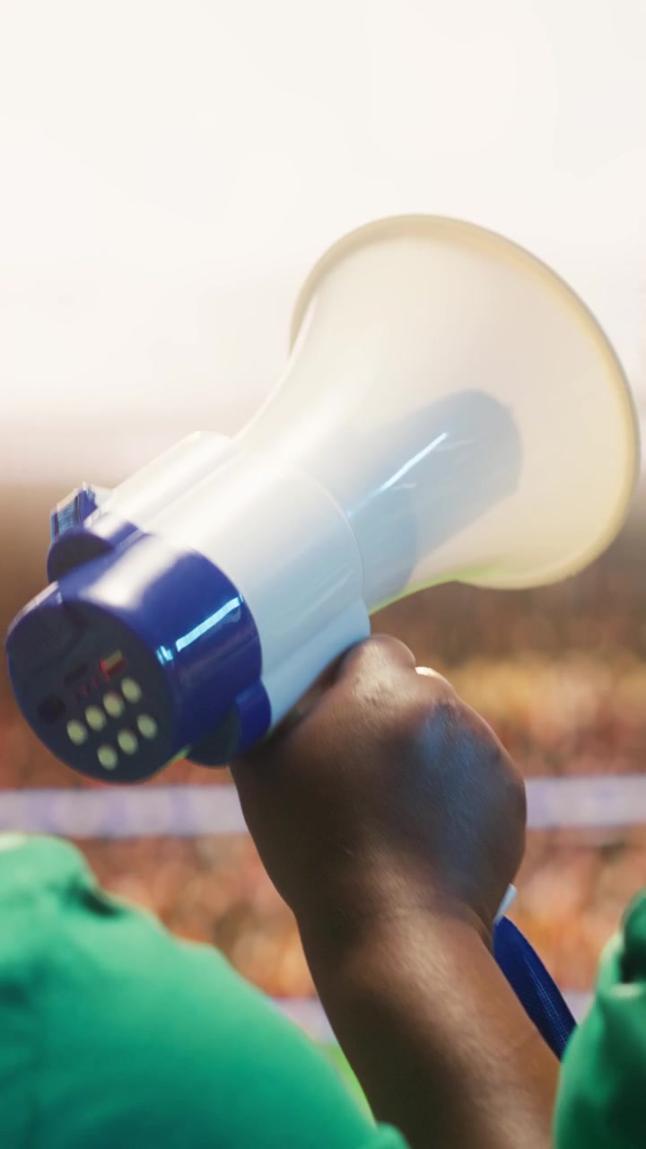 Video verticale. Tifosi di calcio intonano cori con megafono in un'arena sportiva gremita.