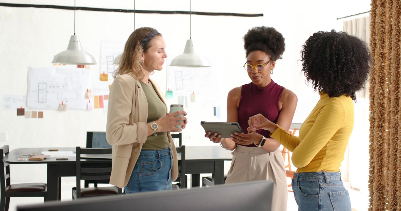 Diverse female coworkers reviewing tablet mockup, pointing, tapping, holding travel mug in office