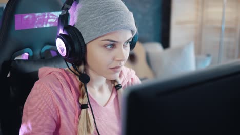 young attractive female vlogger with  headphones playing video games on the computer at home. zoom out