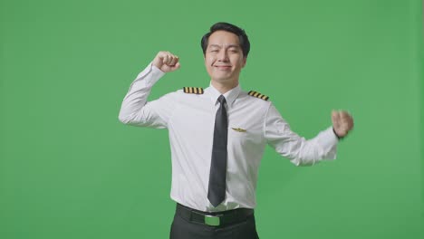 asian man pilot smiling and flexing his bicep while standing in the green screen background studio