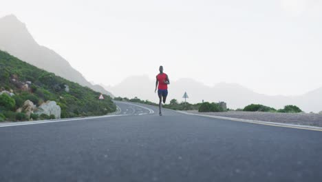 uomo afroamericano in forma che si esercita correndo su una strada di campagna vicino alle montagne