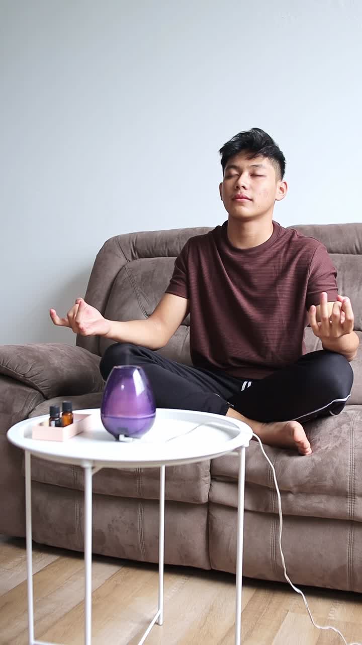 Young man meditating on a couch with diffuser and essential oils on the table