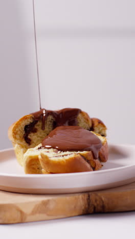 vertical video close up of melted chocolate sauce poured onto chocolate babka bun on plate 1