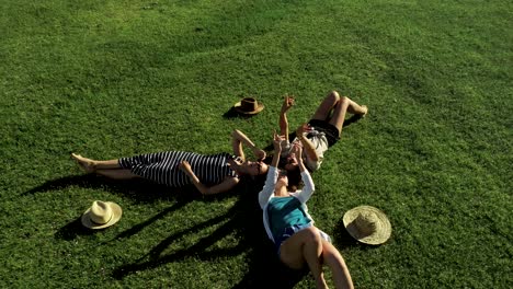 tres chicas atractivas acostadas en la hierba verde y divirtiéndose en un prado día soleado y fondo de montaña