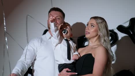 loving caucasian parents with their beloved baby in studio. little kid sucking a pacifier pulls the balloon string.