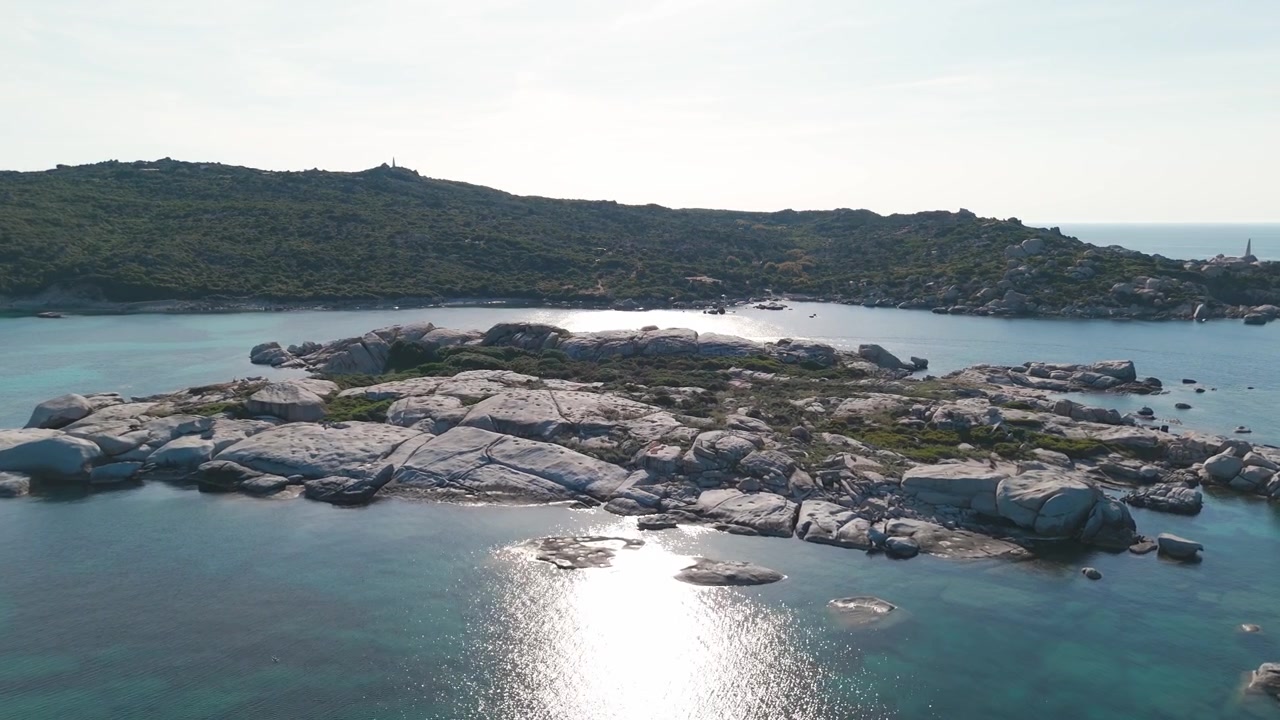 Vista aerea di una costa rocciosa dell'isola con acqua cristallina e riflesso del sole.