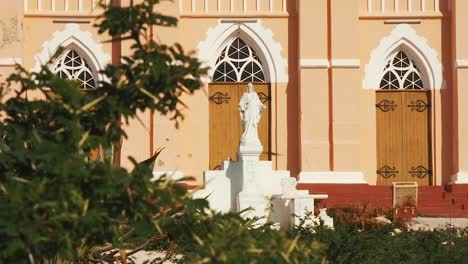 a stunning scenery of statue of jesus christ in front sint willibrordus church with glorious trees on a sunny day in curacao - close up shot