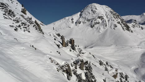 無人機拍攝,隨著雪覆蓋的山坡和岩石頂峰向前移動,向一座大山,在法國的la plagne可以看到滑雪道