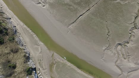 Aerial-top-down-view-of-a-coastal-bay-in-the-north-west-of-England-at-low-tide,-with-a-dog-running-in-the-shallow-waters