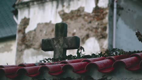 a weathered stone cross behind a wall covered in red tiles