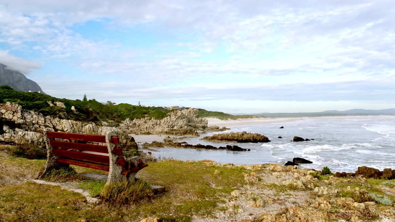 Bænk på Hermanus' kystlinje med udsigt til Grotto og sandede bugter langs den klippefyldte kystlinje.
