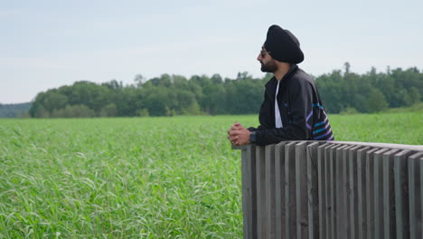 indian man in sunglasses looking at the field with green crops
