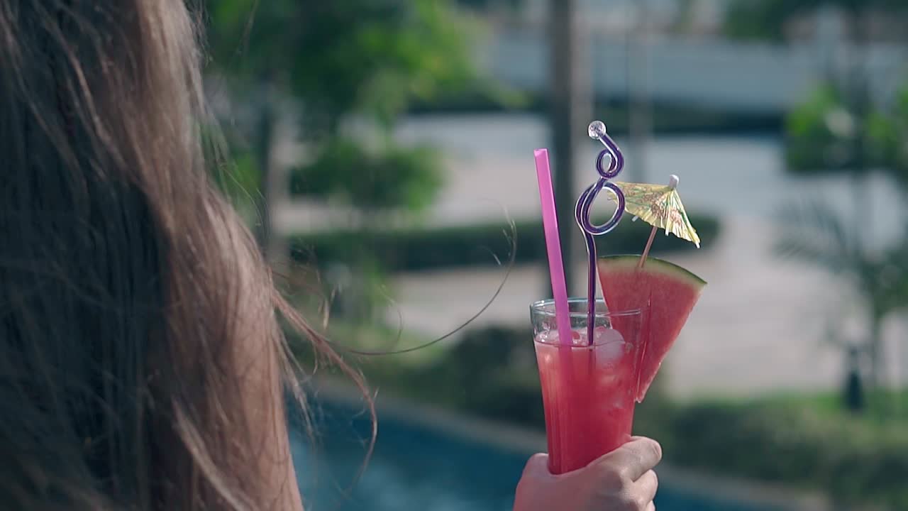 긴 머리카락을 가진 젊은 여성은 분홍색 음료로 높은 잔을 들고 있습니다.