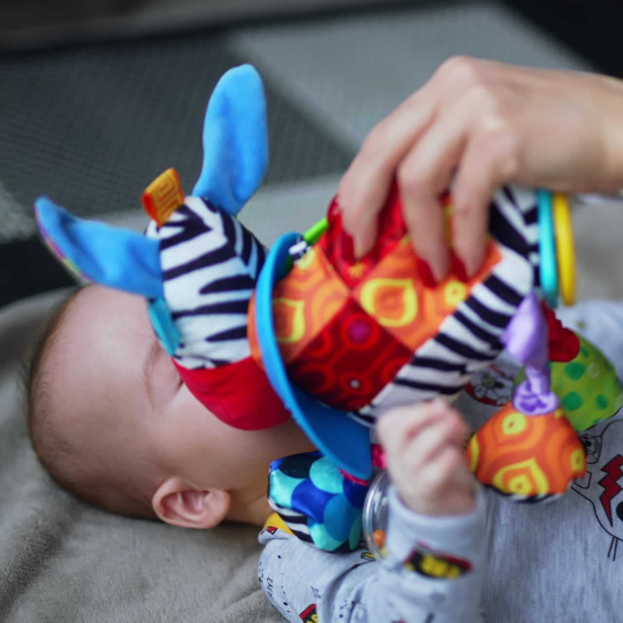 Playful little boy attracted by a colorful soft toy. Mother showing a bright toy to her infant baby. Close up