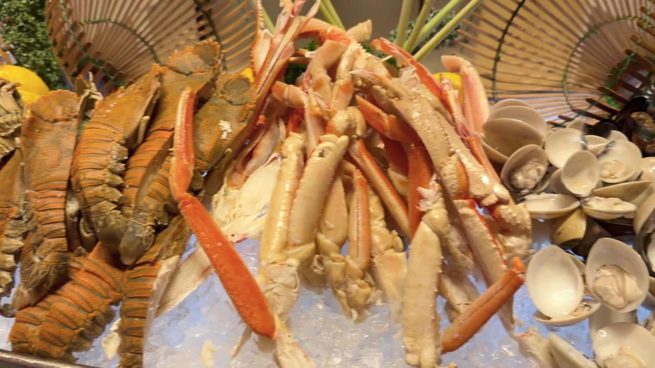 Una lenta panoramica su un espositore refrigerato di frutti di mare che include zampe di granchio, aragoste e vongole.