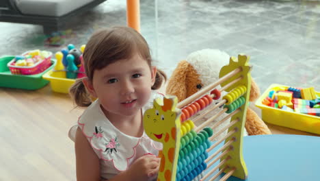 3-year-old little girl playing with educational kids abacus toy which encourages math skills pattern and color recognition, counting addition subtraction maths for early learners