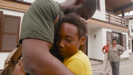 Boy-Embracing-His-Military-Father-And-Saying-Goodbye-To-Him-While-In-The-Distance-His-Mother-And-Grandma-Looking-At-Them