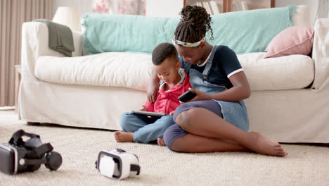 african american sister and brother using tablet and smartphone in living room, slow motion