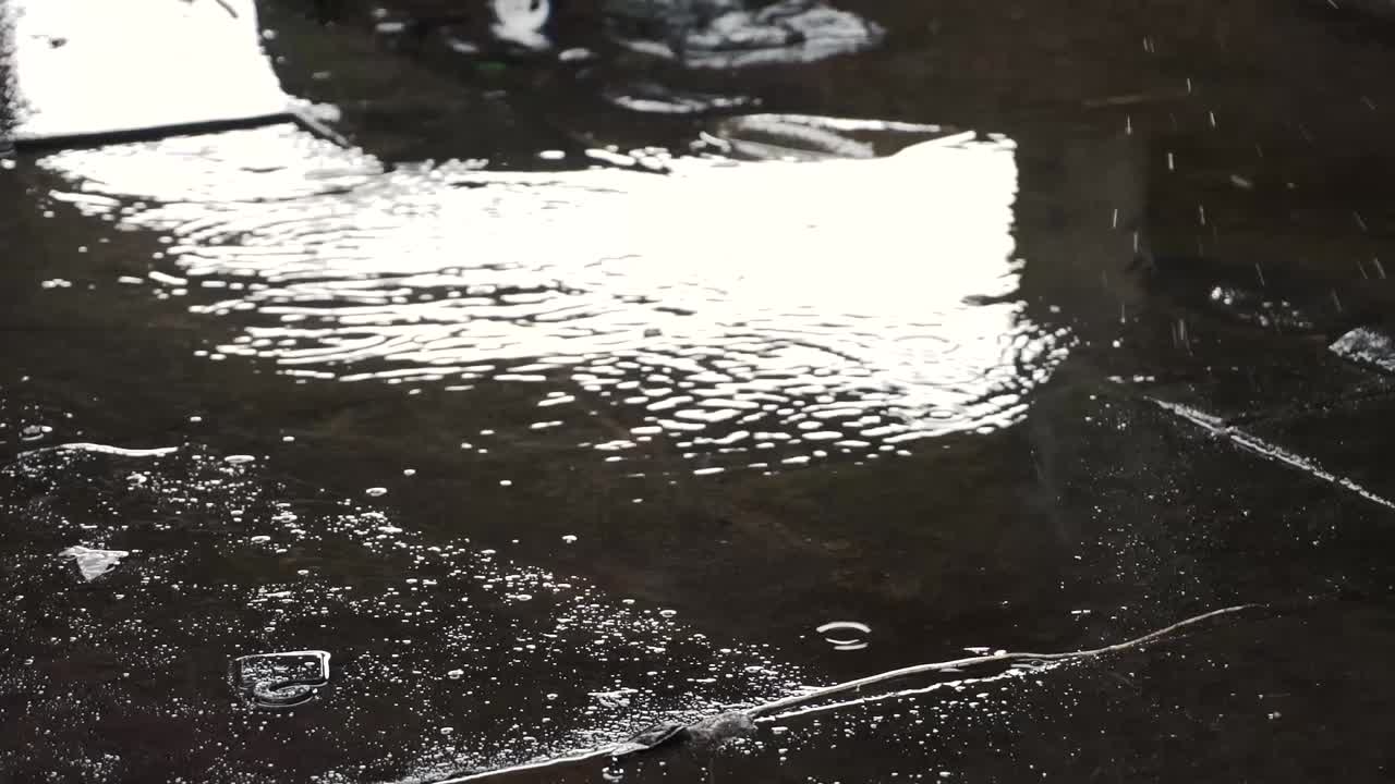 Vanddråber fra regn, der rammer vandpyt under broen.