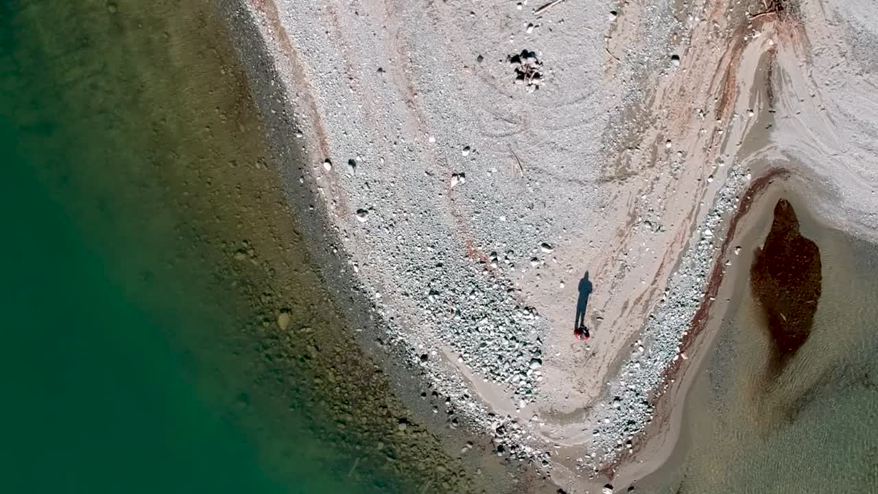 Drone shot looking down and moving down at man and shadow on sand bar with abstract shapes and color.