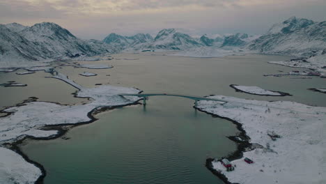 Winterliche-Seebrücke-Zwischen-Ramberg-Dorf-Auf-Verschneiten-Lofoten-Nordland-Gletscherinsel-Luft-Absteigend