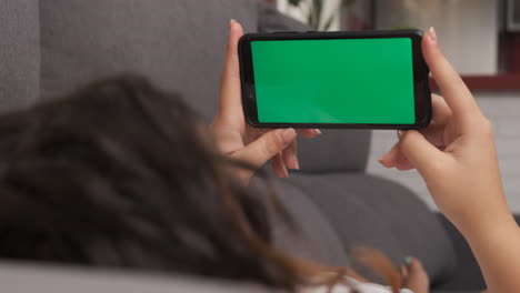 mujer en el sofá de la sala de estar viendo algo en su teléfono celular, pantalla verde en el teléfono inteligente
