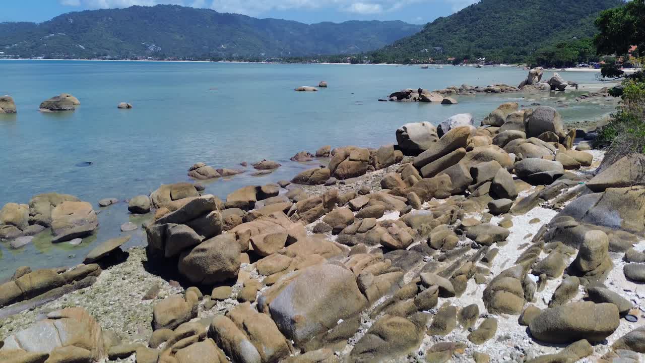 Aerial drone footage of Lamai Beach in Koh Samui, Thailand, featuring turquoise ocean, rocky shoreline, tropical island horizon, and scenic coastal landscape under clear tropical skies