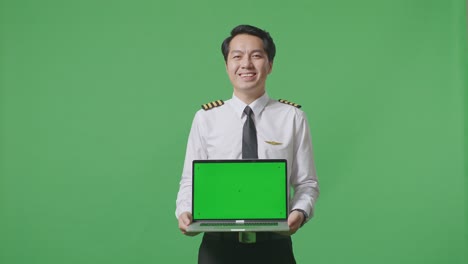 asian man pilot smiling and showing green screen laptop to the camera while standing in the green screen background studio