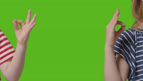 close up of two young children making meditation mudra gesture to camera against green screen