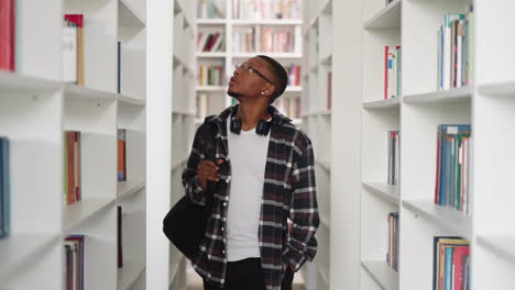 young student looks around in college library. african american man in checkered shirt seeks textbooks in store. informational sources storage