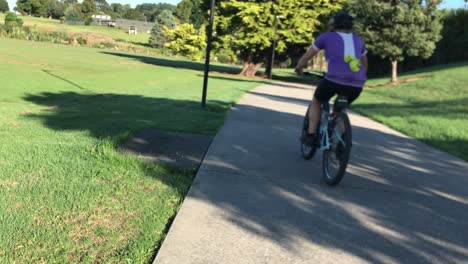 cyclist riding at a quick pace down a concrete pathway in a park