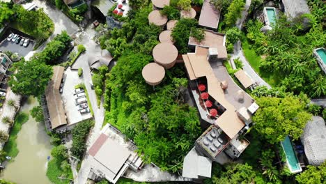 Establishing-shot-of-beautiful-and-luxurious-resort-with-cars-parked-at-entrance-and-hut-theme-villas-with-swimming-pool-and-sparkling-water-surrounded-by-trees-and-greenery