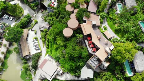 establishing shot of beautiful and luxurious resort with cars parked at entrance and hut theme villas with swimming pool and sparkling water surrounded by trees and greenery