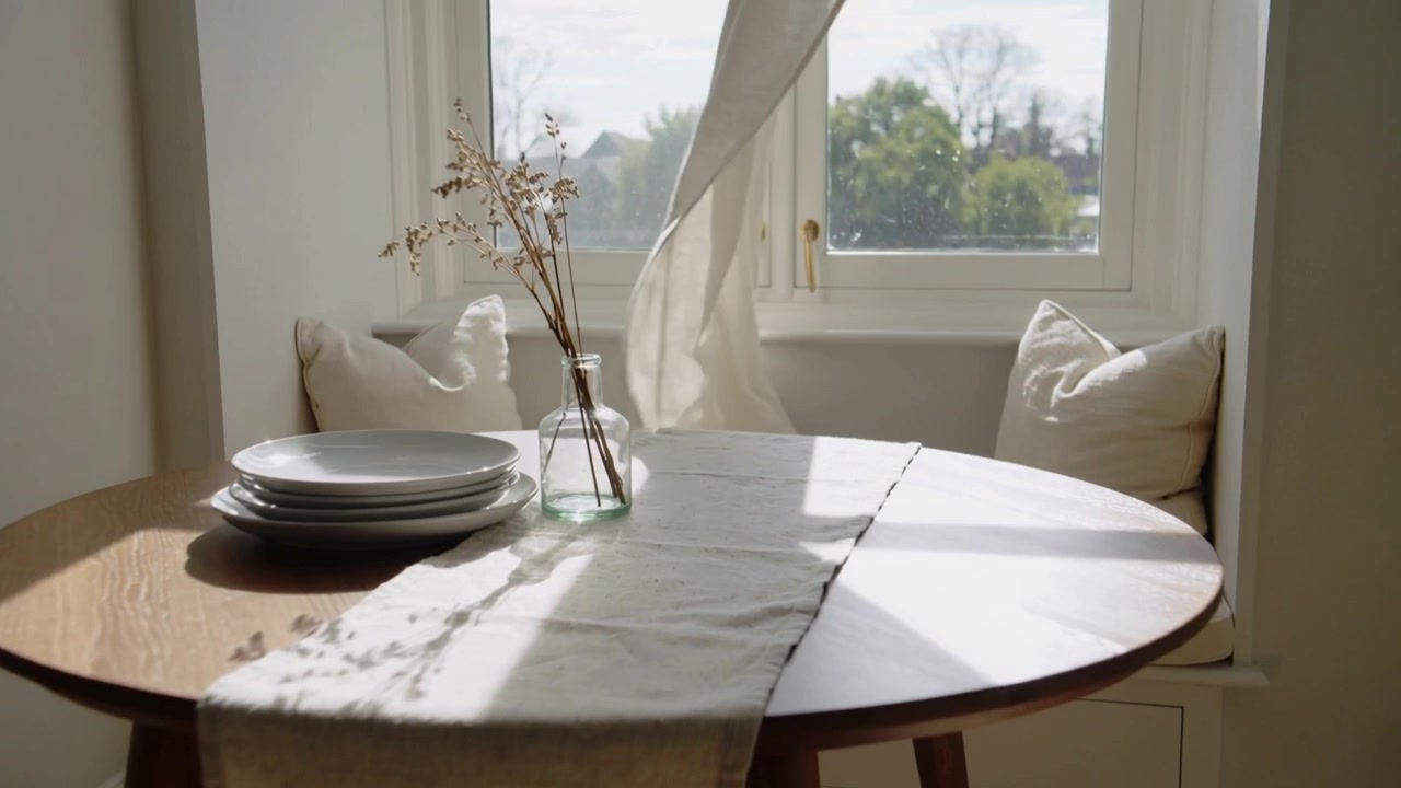Moving gentle breeze entering window, billowing sheer curtain across round table, swaying vase