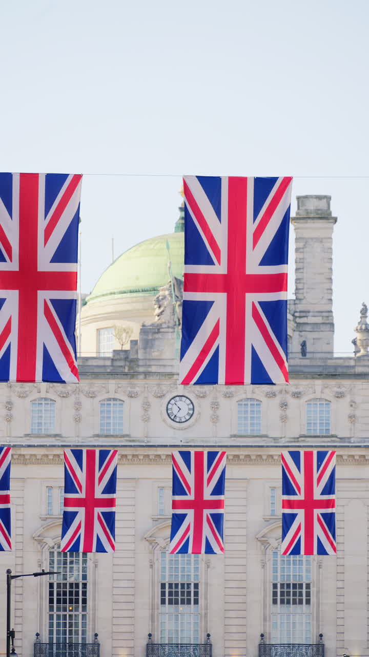 Multiple flags of the United Kingdom hanging proudly above a busy city street in central London. Vertical