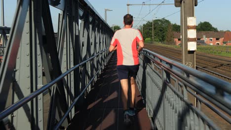 following middle aged male trail runner on steel bridge between train tracks and asphalt road