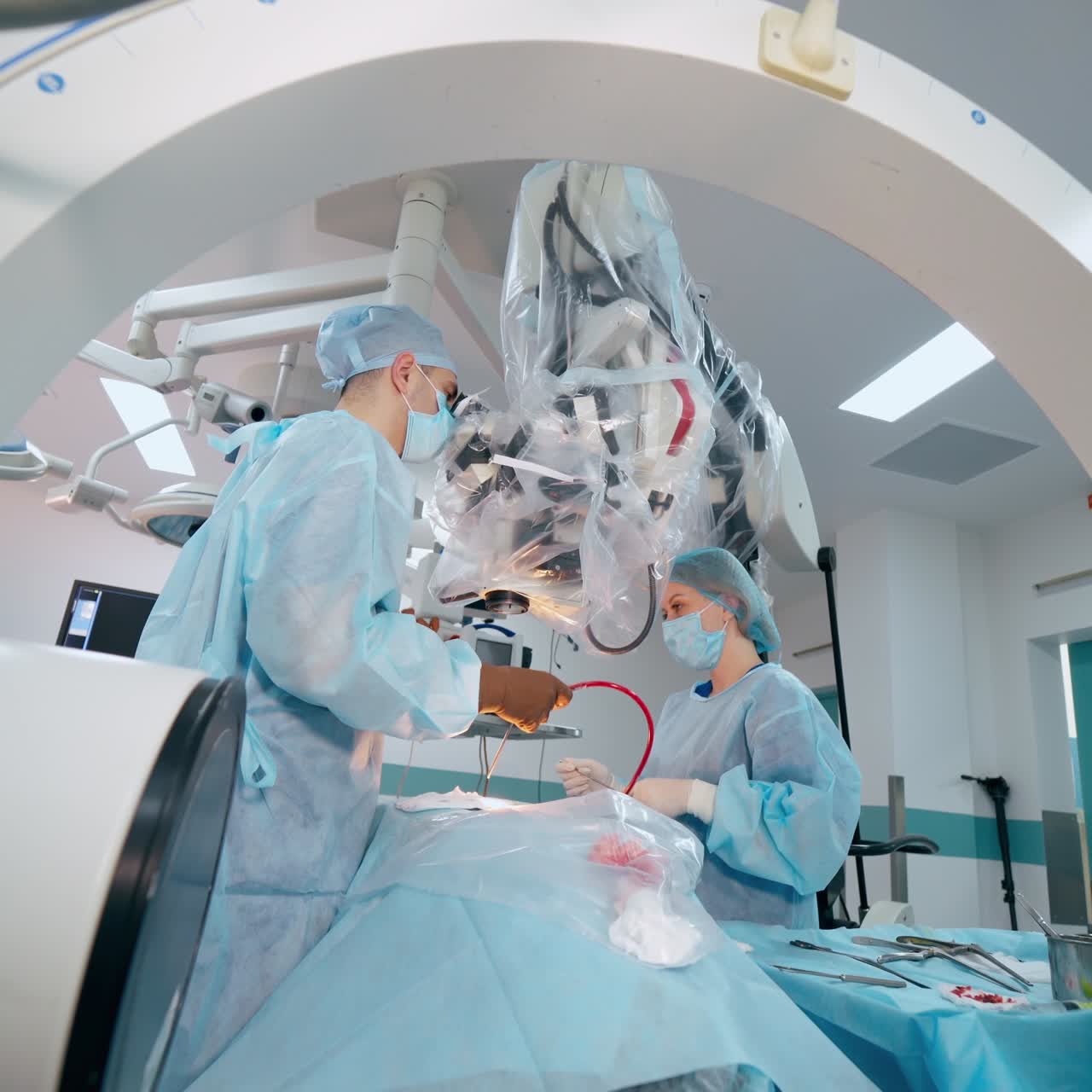 Surgeon and a nurse in the operating room. Patient is under anesthesia on a surgical table. Specialists using modern equipment during neurosurgery.