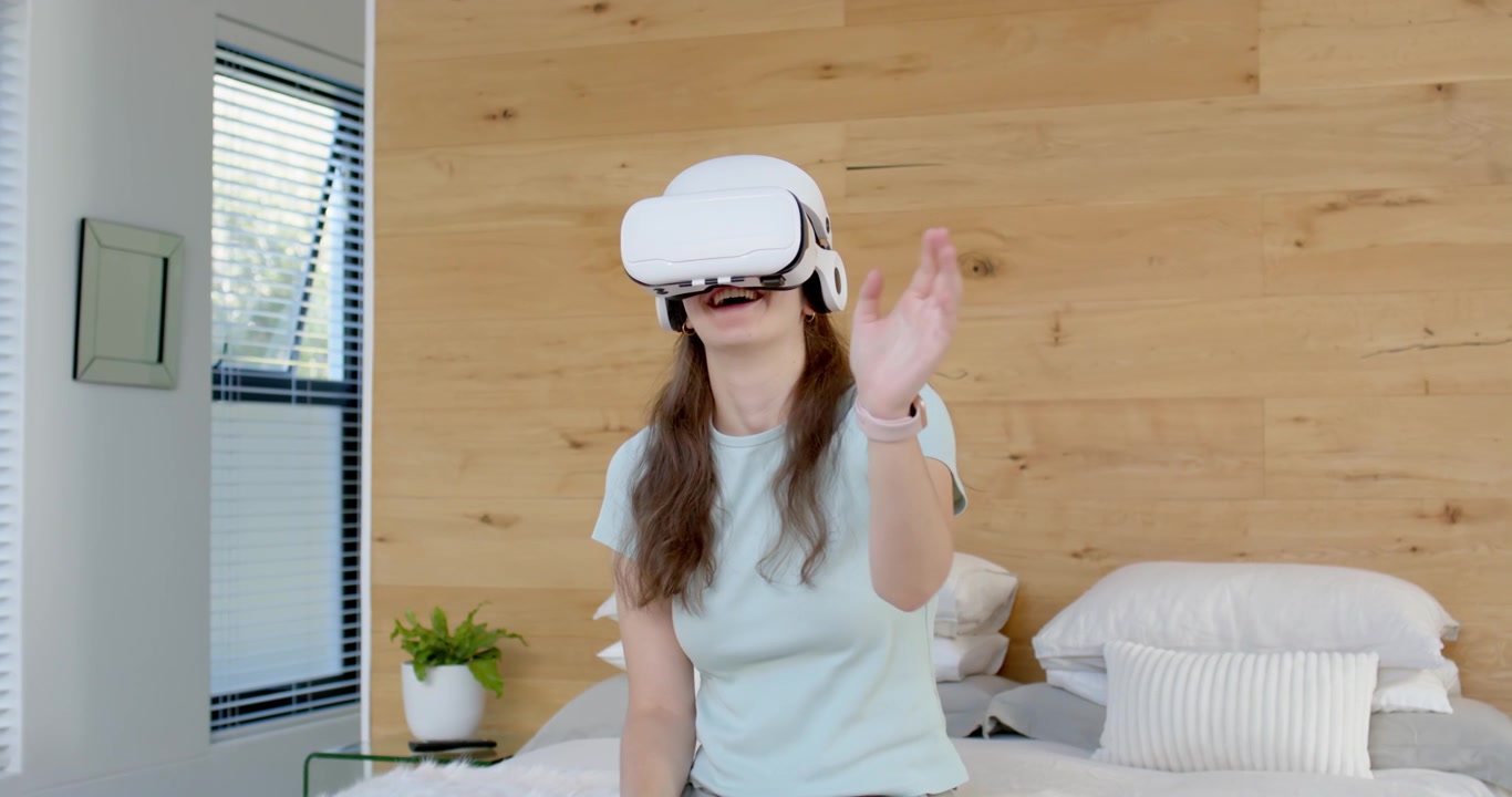 Donna adulta seduta in camera da letto sul letto, che indossa un visore VR bianco e uno smartwatch, mentre naviga nel menu VR.